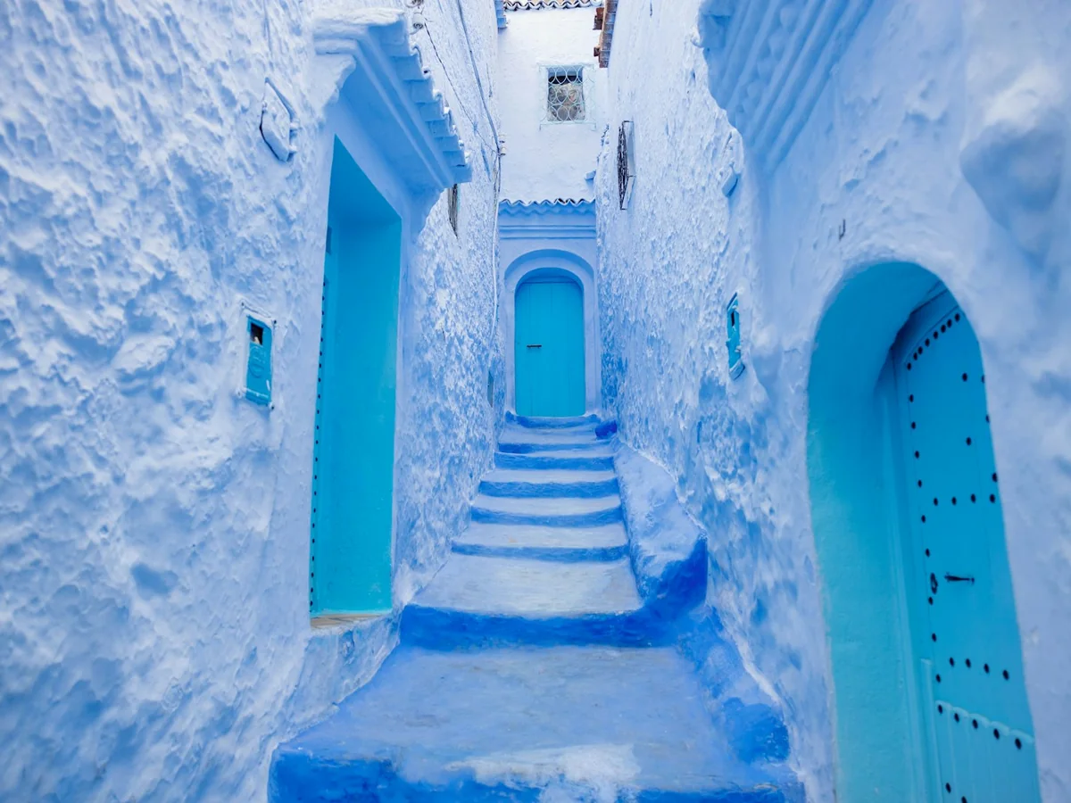 A narrow stepped alley in Chefchaouen's medina, its walls painted indigo blue with turquoise doors